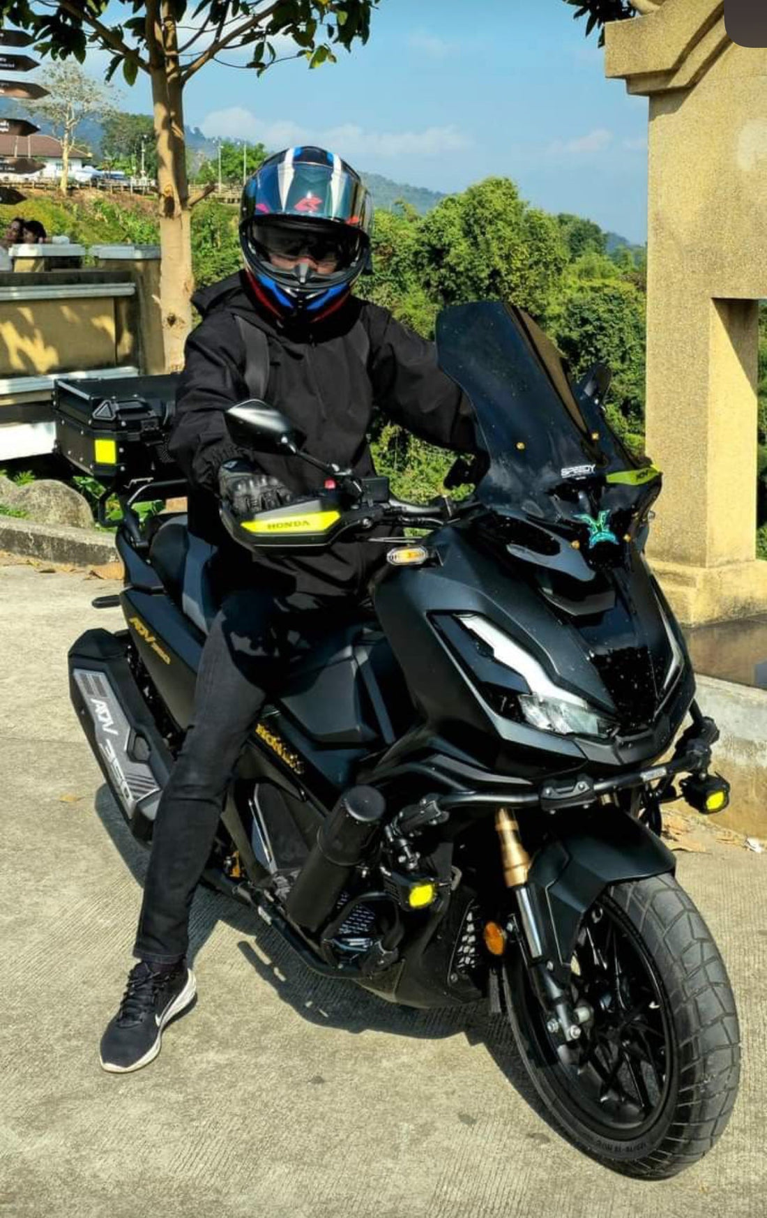 homme sur une moto qui est sur une route avec des abres en arriere plan la moto est équipée d'accessoires noga top case aluminium et feux additionnels evo