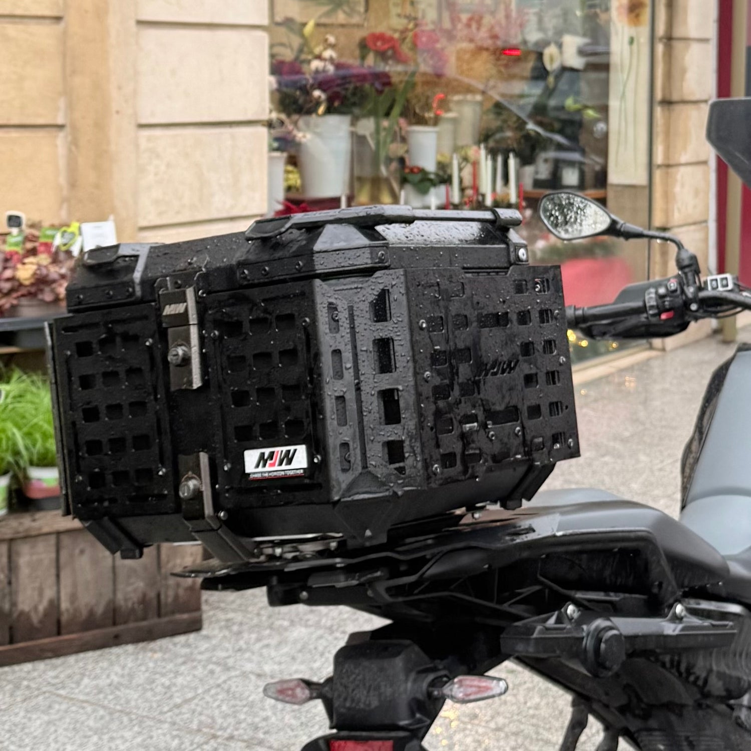 photo réelle qui met en avant un top case NOGA adventure 55L sur un gs1300 BMW sous la plue en pleine rue en ville